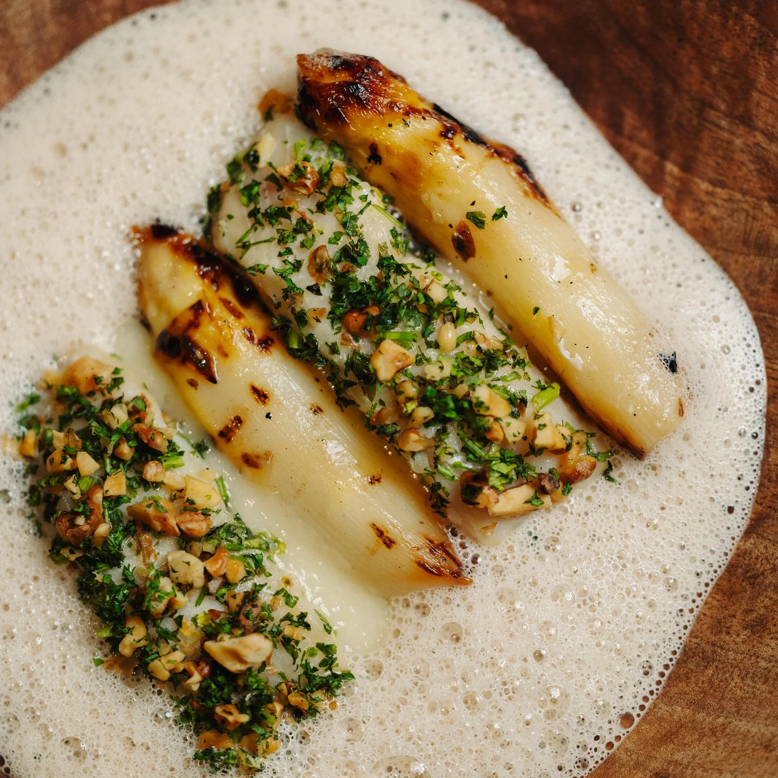 Asperges grillées garnies de persil et de noix, disposées sur une sauce blanche dans une assiette en céramique