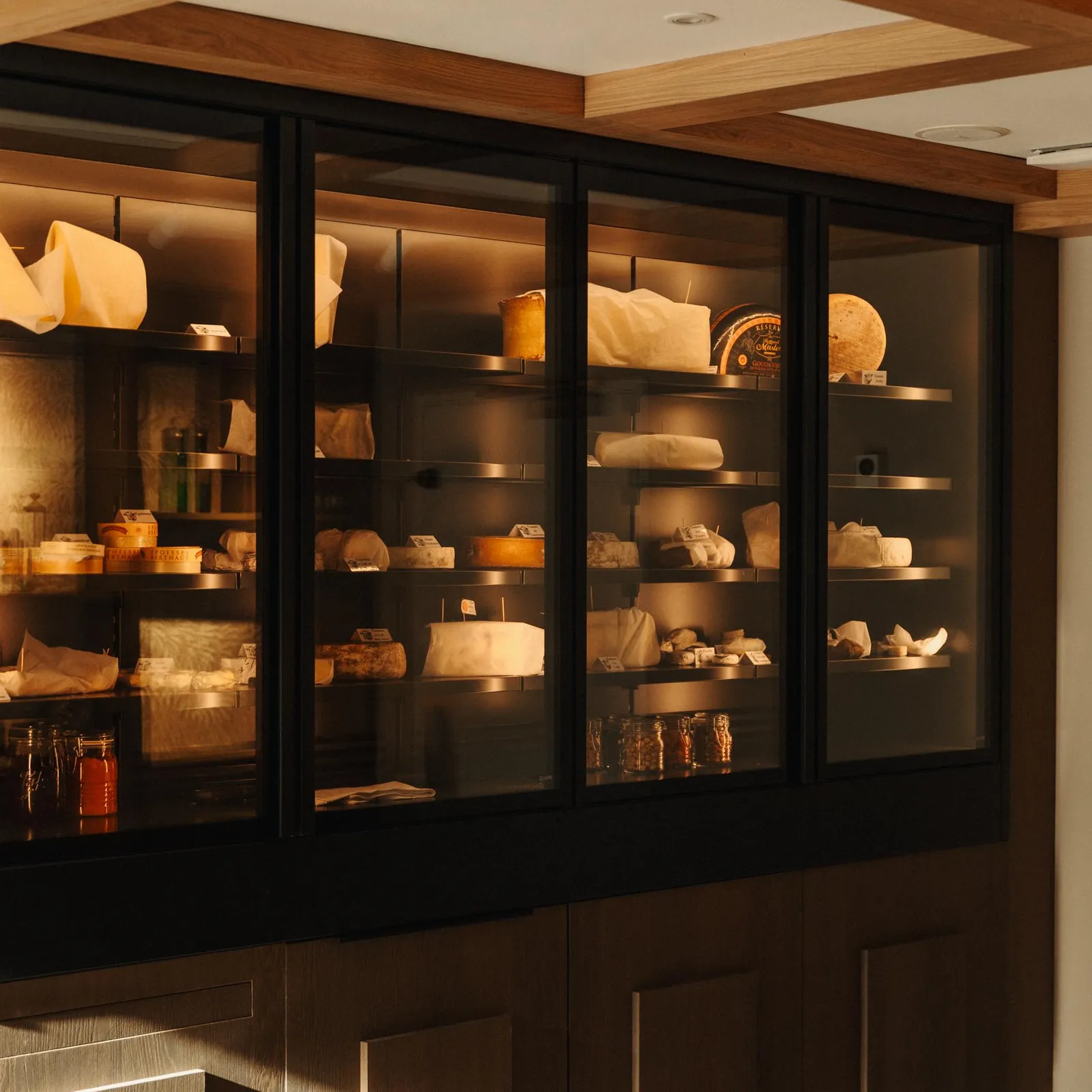 Une vitrine en verre noir expose divers fromages et condiments sur des étagères éclairées