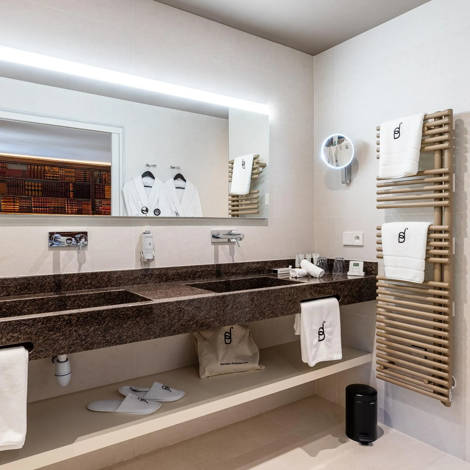 Salle de bain moderne avec double vasque, miroir, serviettes et peignoirs suspendus, et porte-savon sur le mur