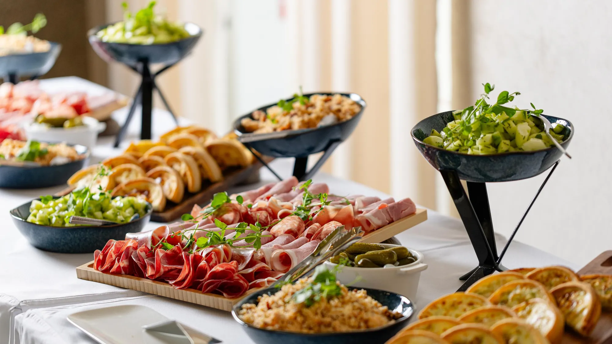An assortment of cold dishes including charcuterie, salads, olives, and bread is presented on a table.