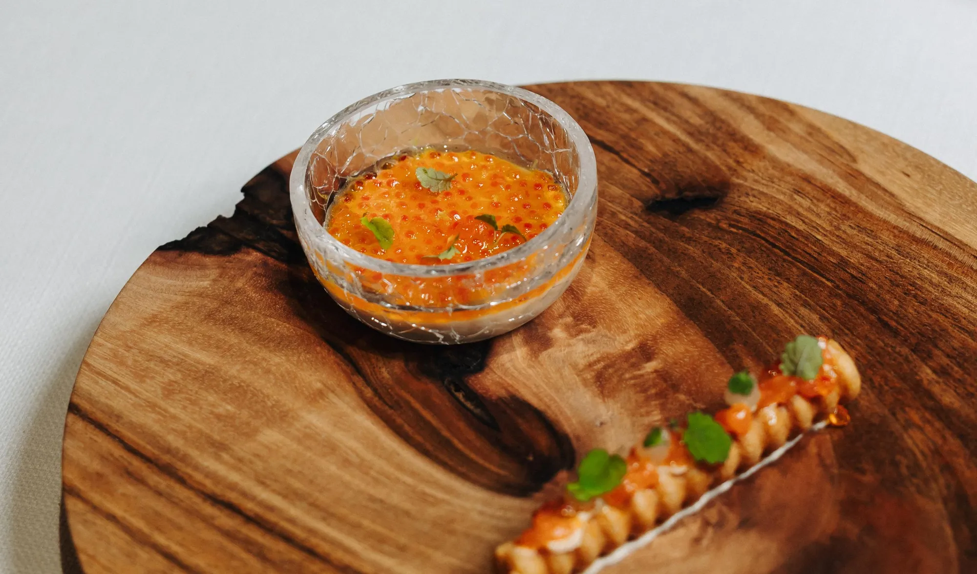 Eine kleine Schüssel mit oranger Sauce, Kräutern und Chilischoten, auf einem Holzbrett mit einer Garnitur Garnelen