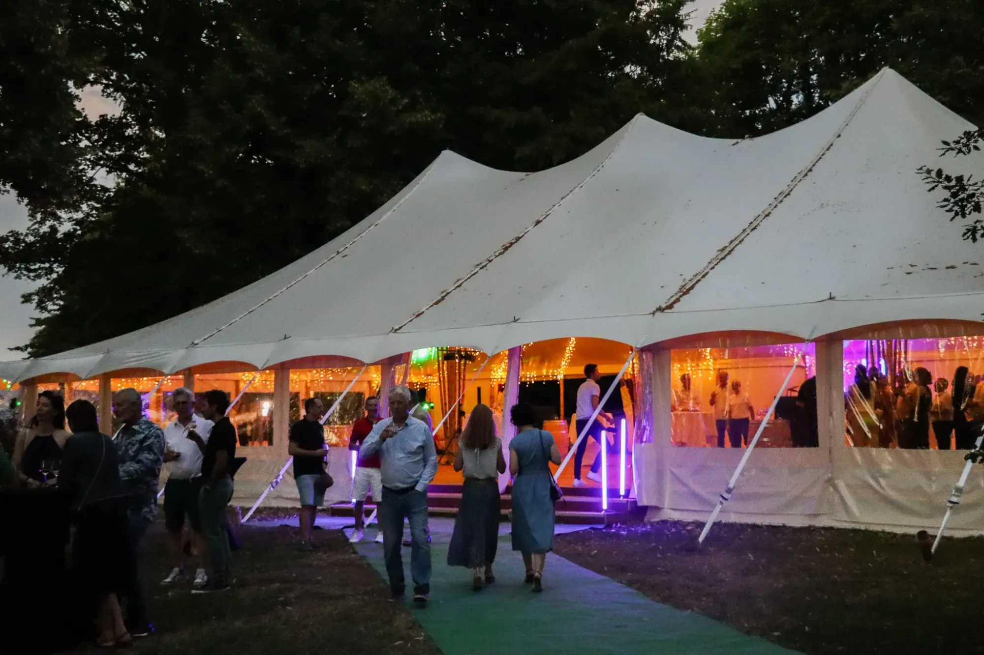 A group of people stands in front of a tent lit with string lights, with a colorful stage inside.