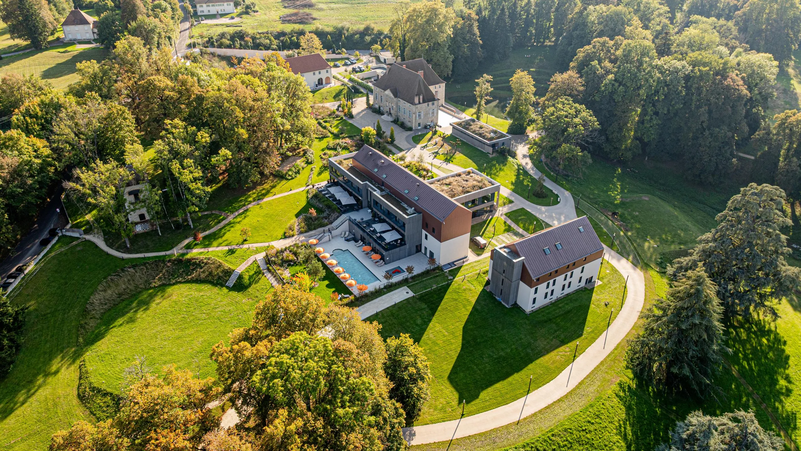 Vue aérienne d'un domaine avec plusieurs bâtiments, des jardins bien entretenus et des chemins sinueux entourés d'arbres