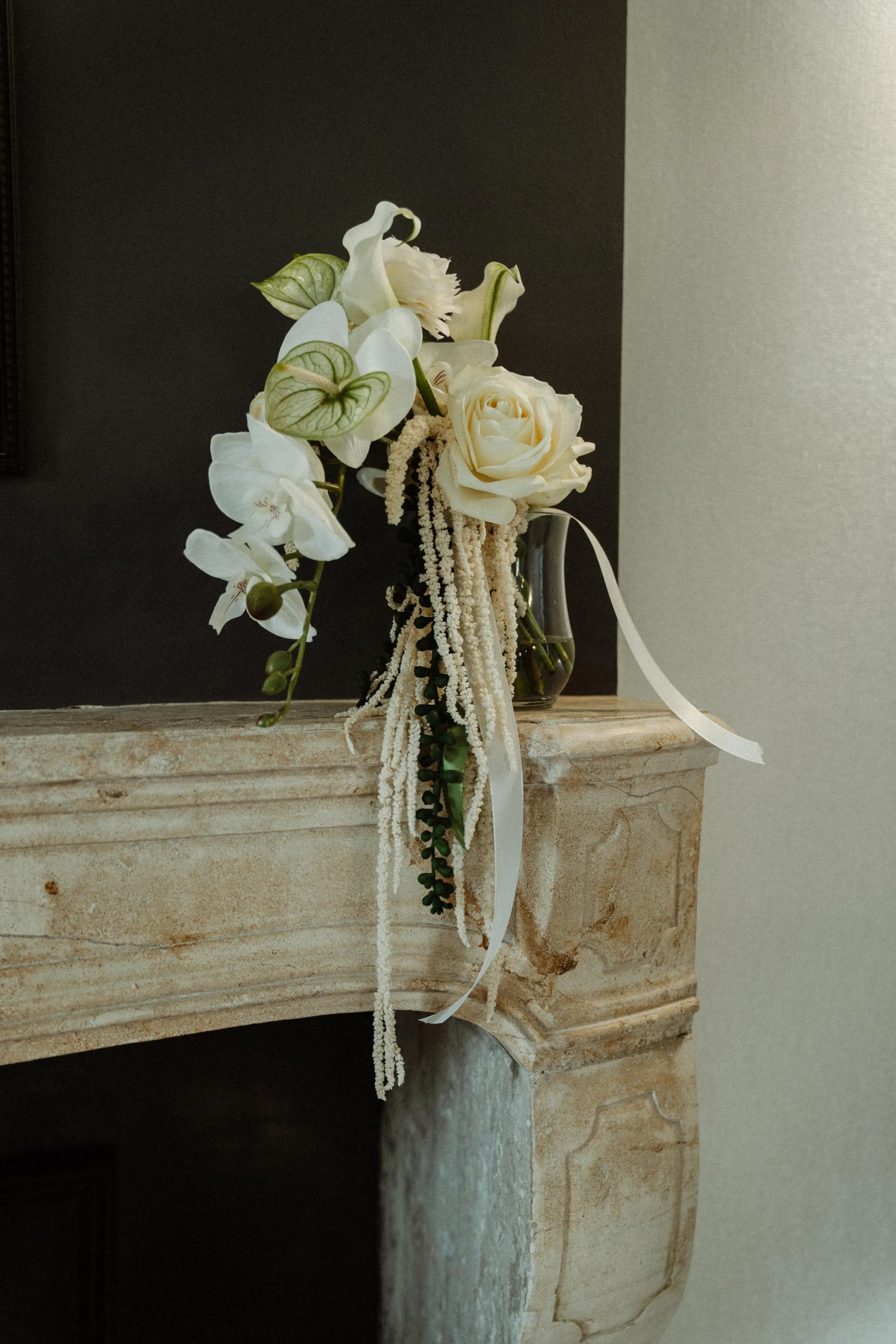 Un vase contenant un bouquet de fleurs blanches et des feuilles vertes posé sur une cheminée en pierre