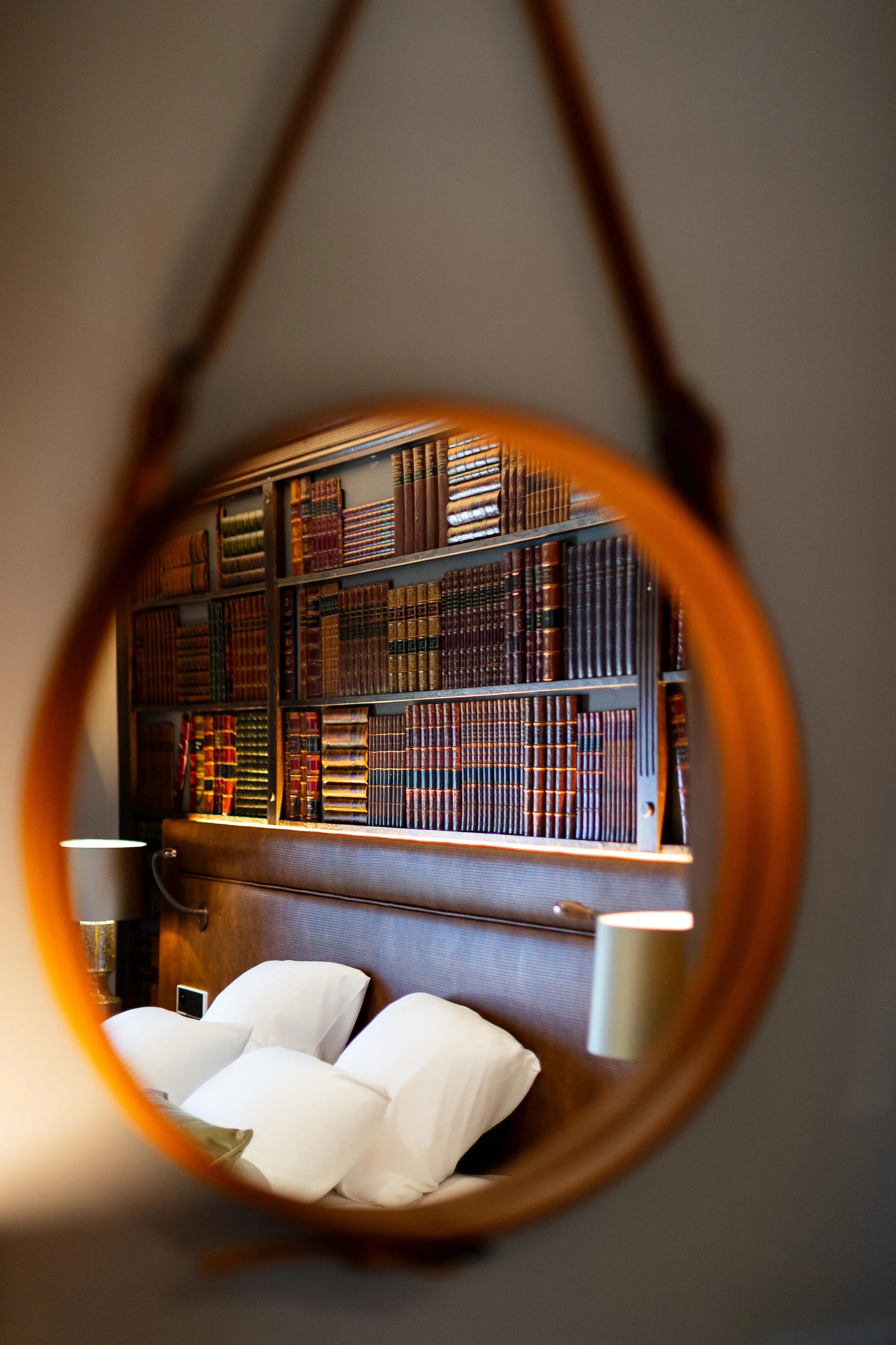 Vue à travers une lentille circulaire d'une étagère remplie de livres anciens et d'un lit avec des oreillers blancs