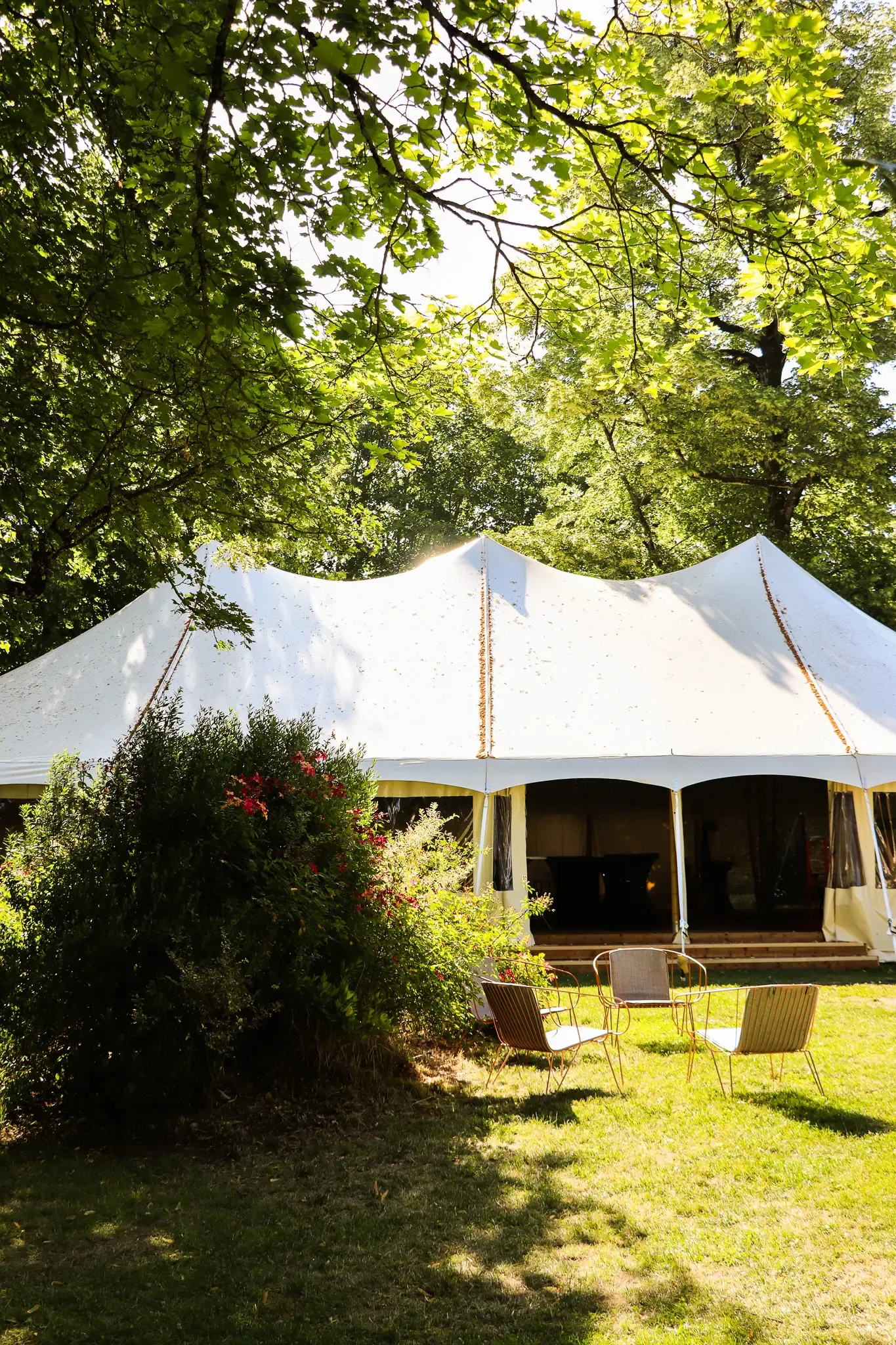 A white tent is set up in a tree-lined garden with chairs arranged in front.