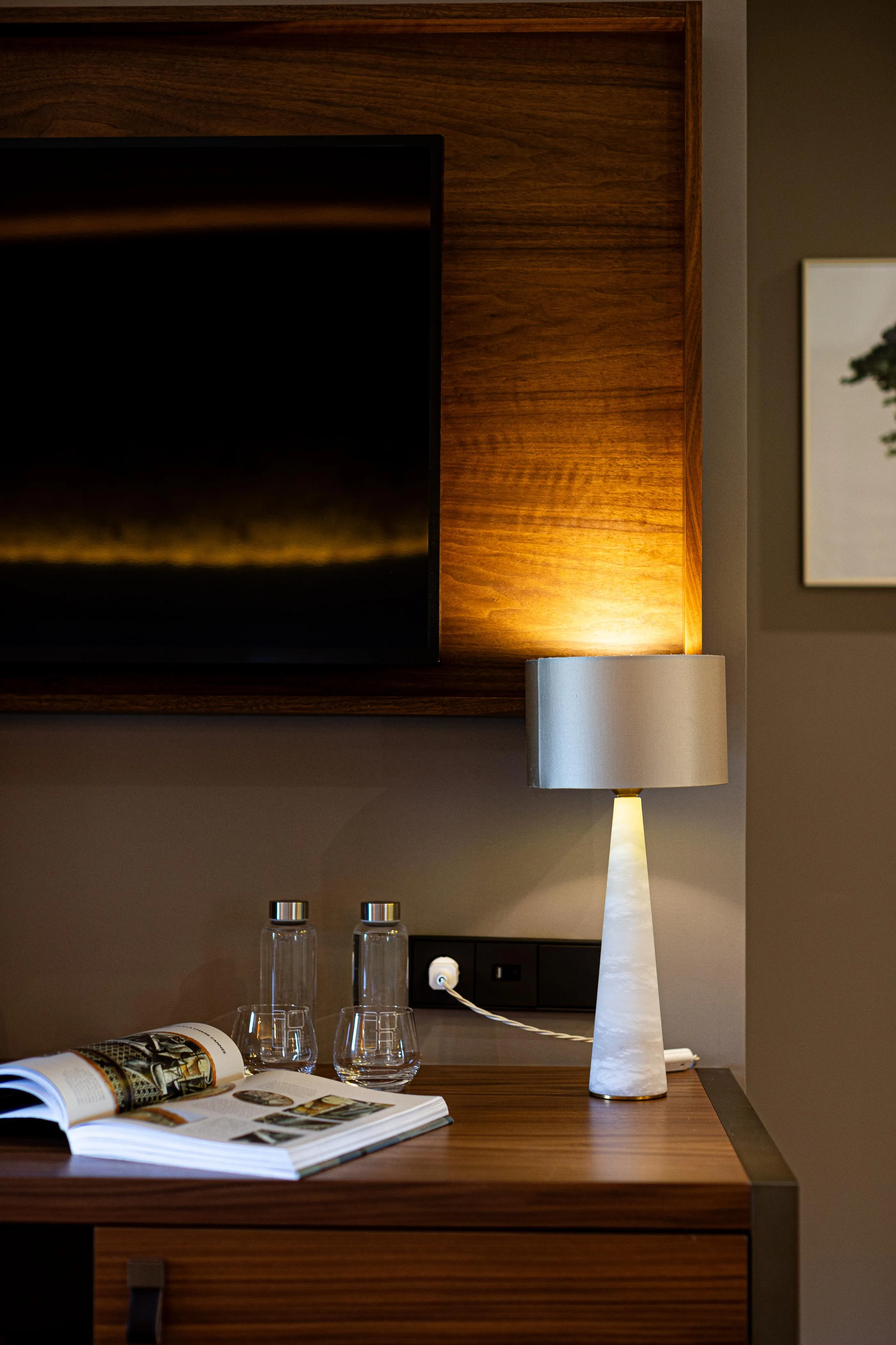 Ein Nachttisch aus Holz mit einer eingeschalteten Lampe, Gläsern und Zeitschriften