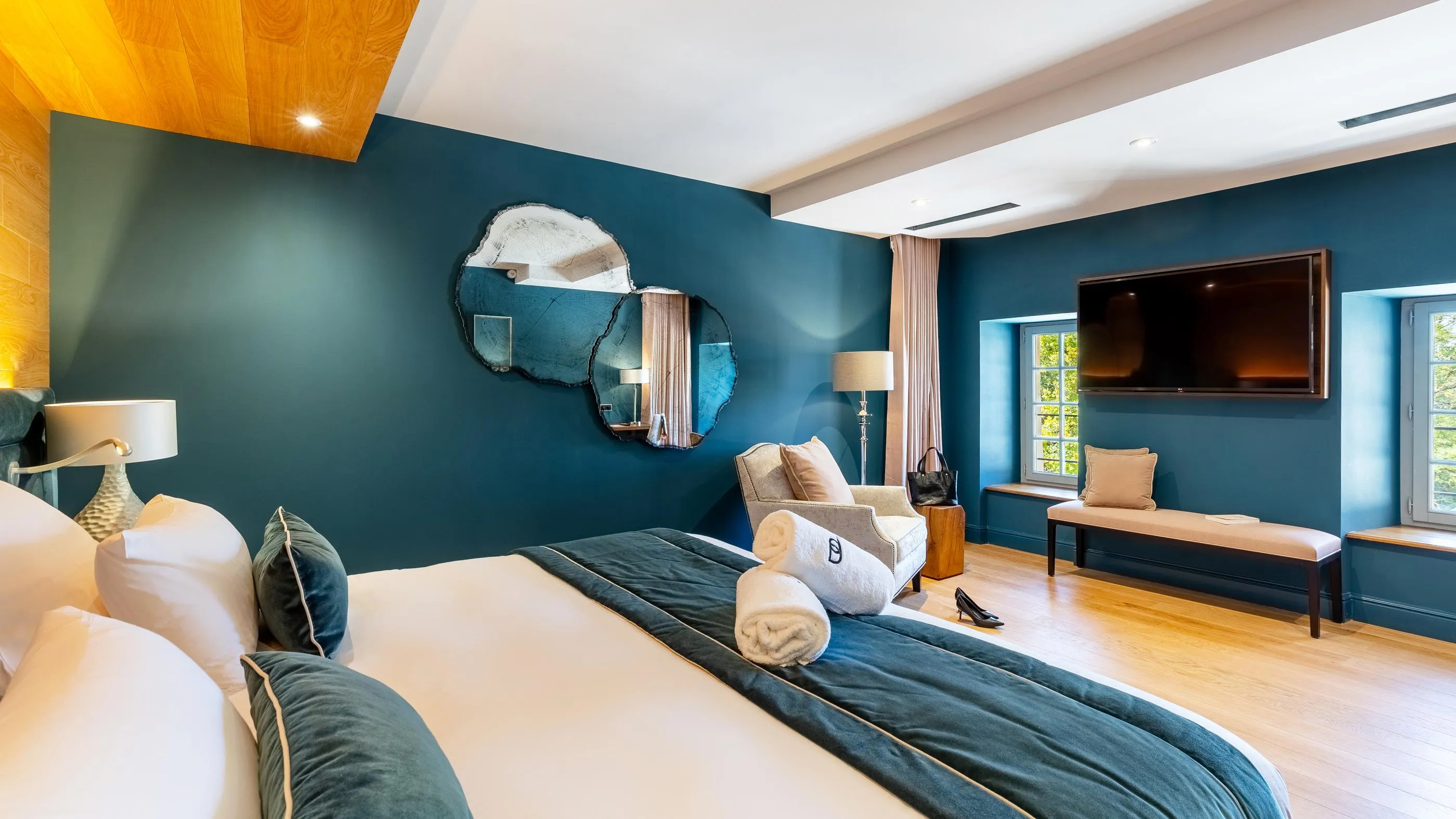 Chambre moderne avec lit, fauteuil, télévision, miroir mural et fenêtres donnant sur l'extérieur