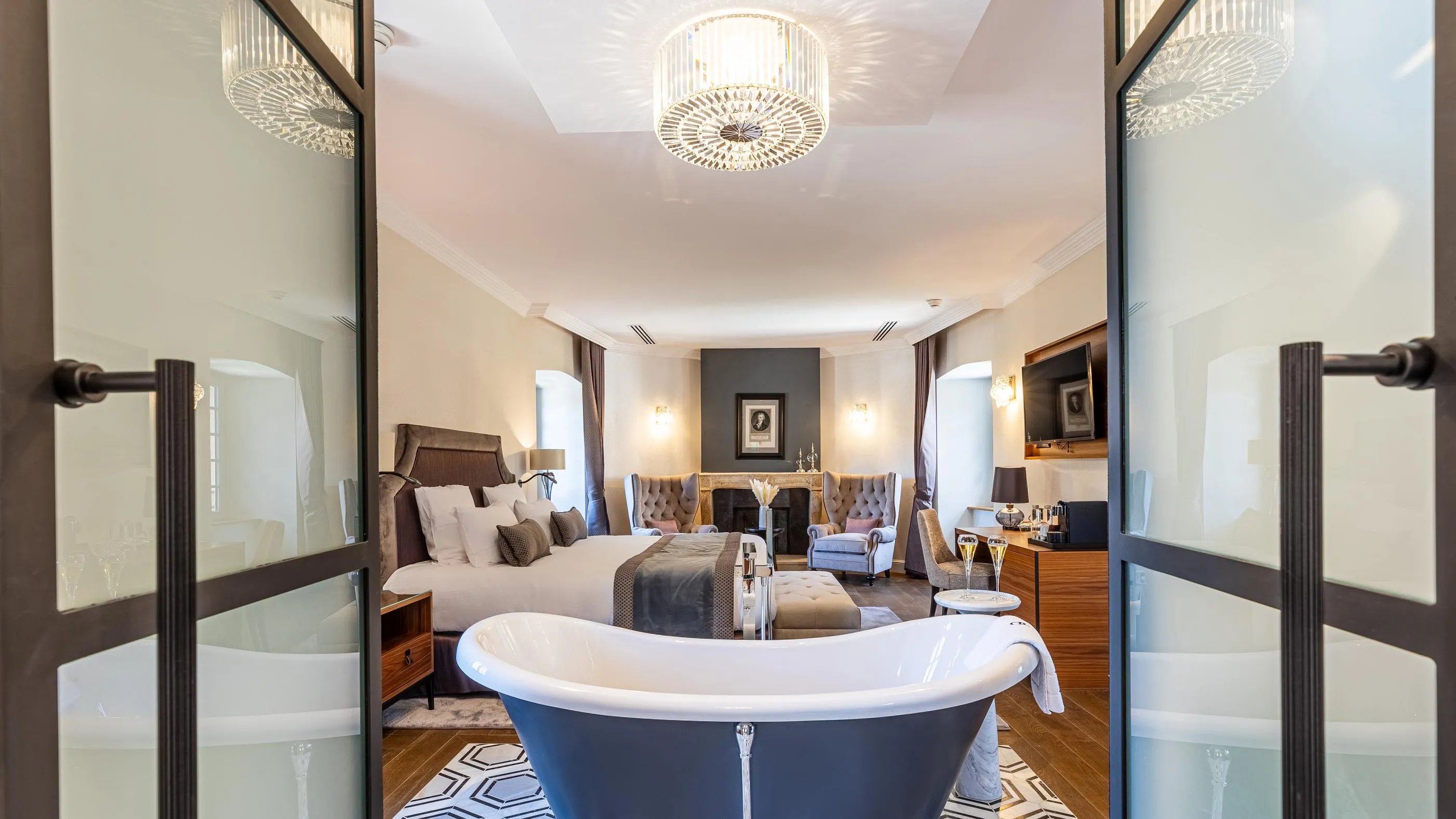 Luxuriöses Zimmer mit einem Bett, einer Badewanne, Kandelabern und Möbeln, Blick durch eine Glastür