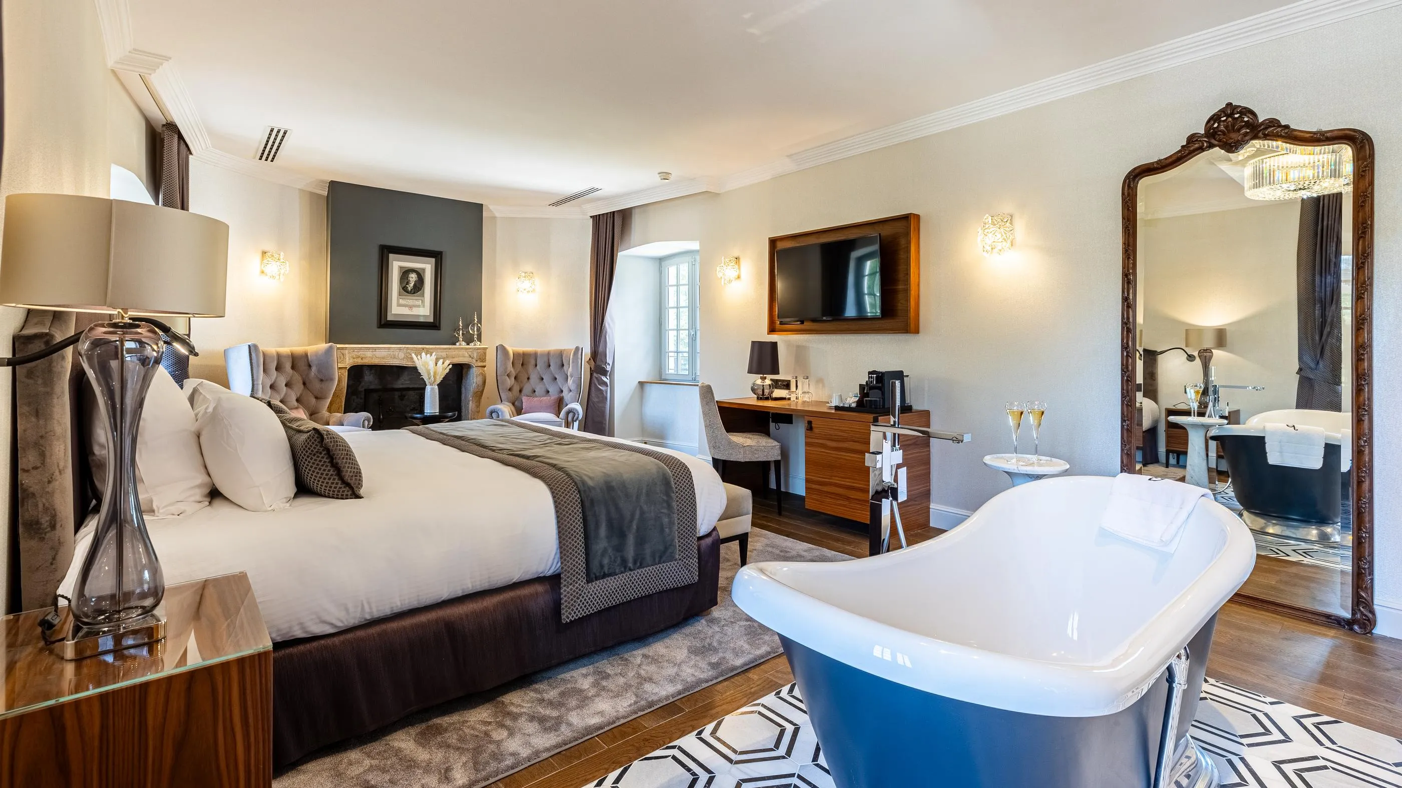 Luxuriöses Zimmer mit einem großen Bett, einer weißen Badewanne, einem Stehspiegel und einem dekorativen Kamin