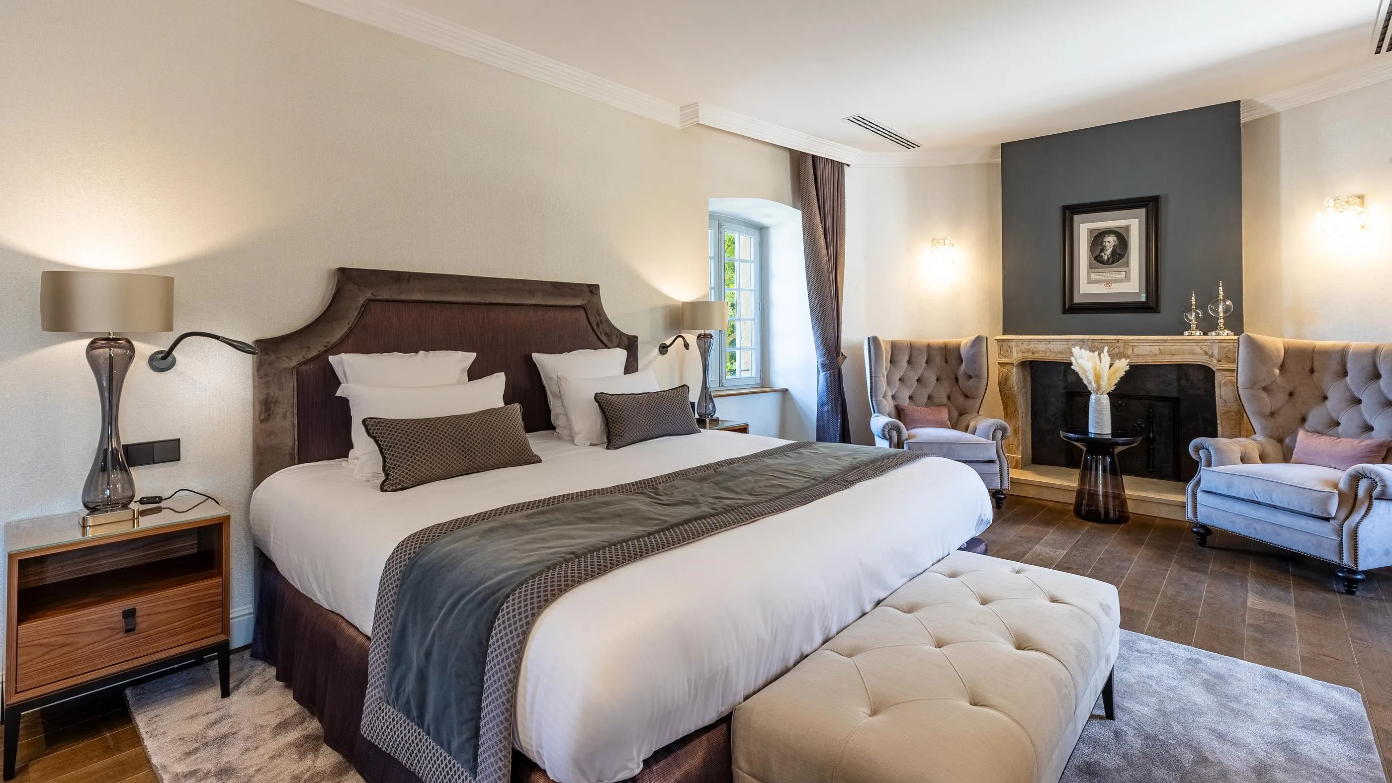 Elegante Zimmer mit einem großen Bett mit Holzkopfteil, einem Kamin, Wandlampen und einem gepolsterten Sessel am Fenster