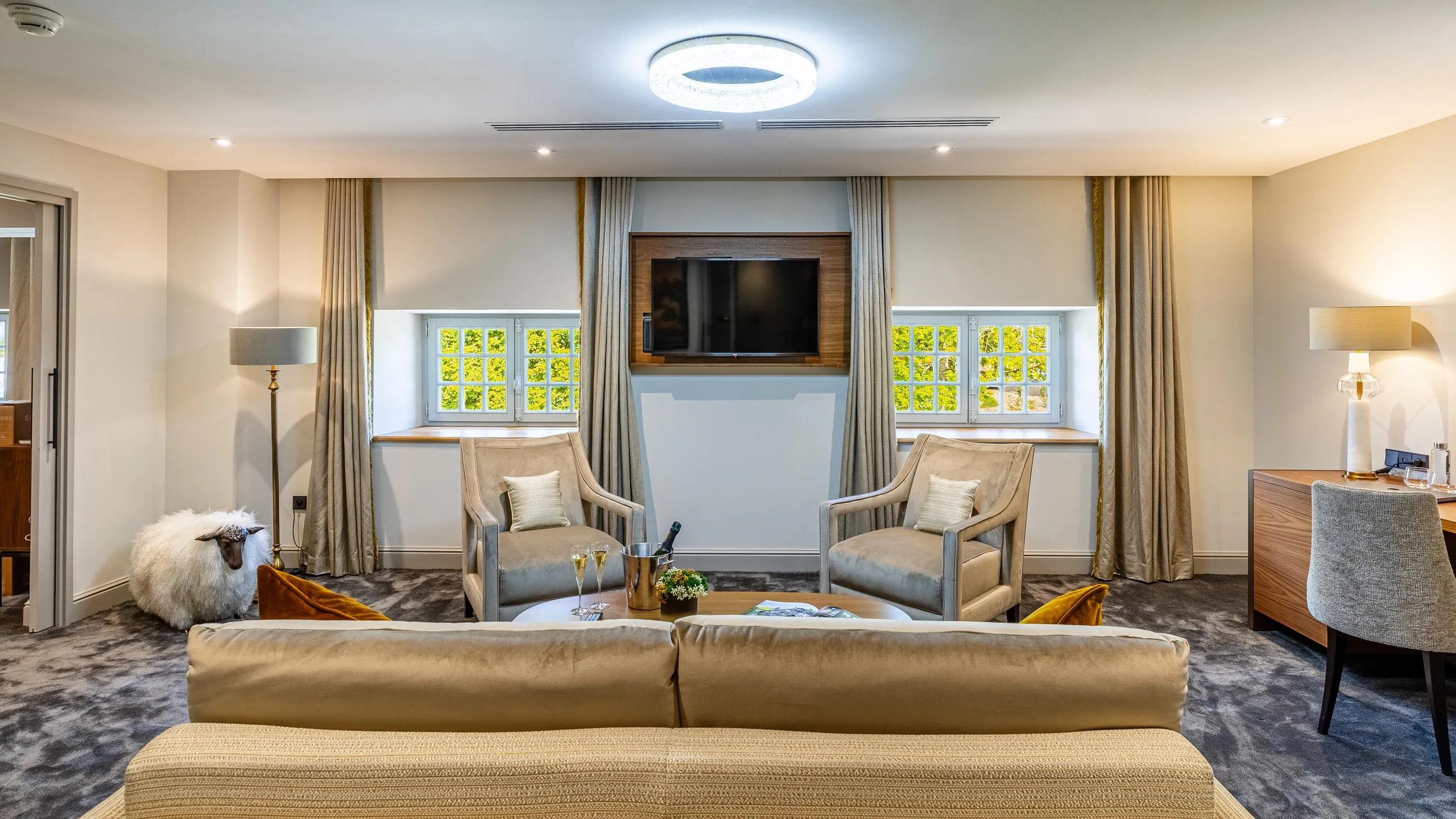 Wohnzimmer mit Sofa, Sesseln, Couchtisch, Lampen und Fenstern mit offenen Vorhängen