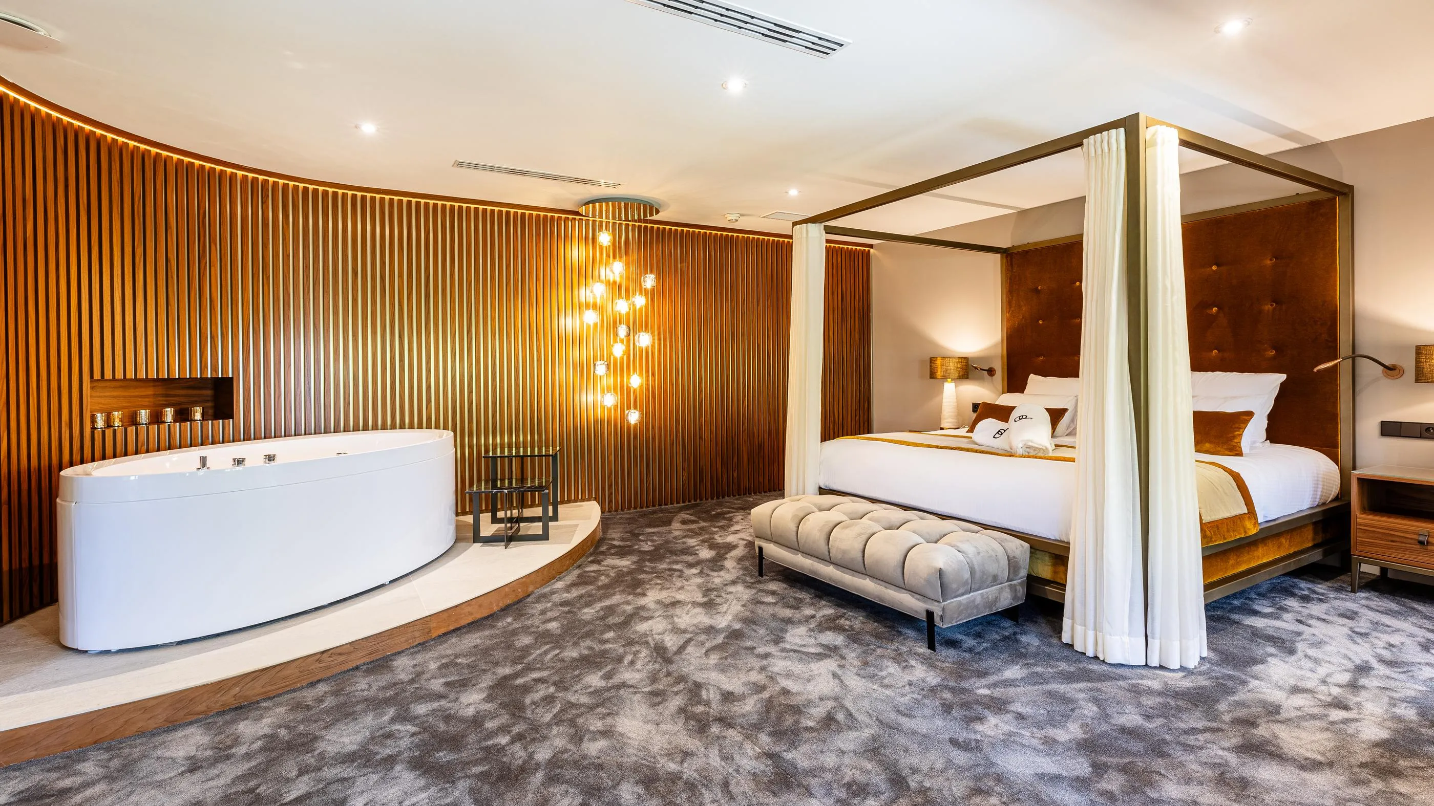 Luxuriöses Zimmer mit einem Himmelbett, einer eingebauten Badewanne und einer mit beleuchteten Holzlatten verzierten Wand