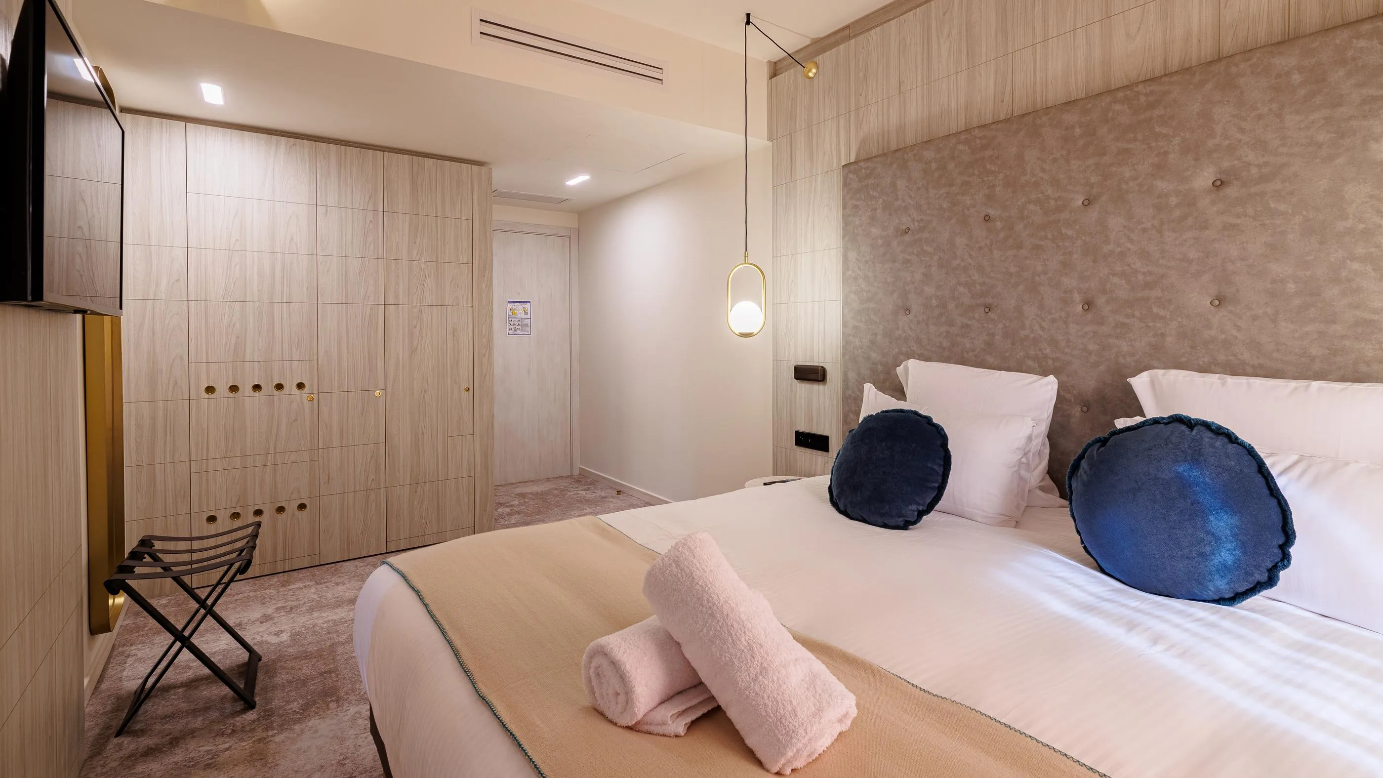 Modernes Hotelzimmer mit Doppelbett, Kissen, Handtüchern und Wandbeleuchtung