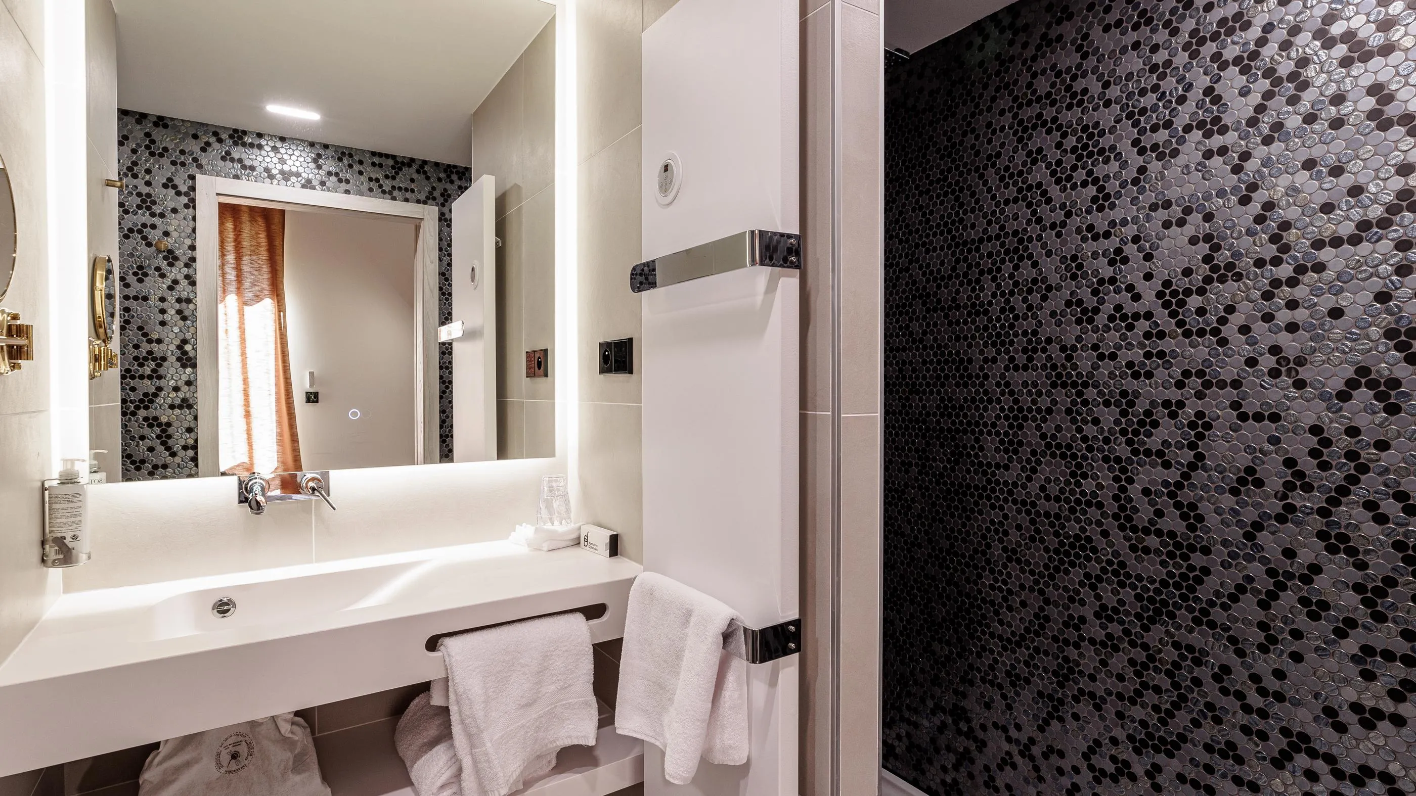 Moderne Badezimmer mit Waschbecken, Spiegel, Handtüchern und einer mit grauen hexagonalen Mosaikfliesen verkleideten Duschabtrennung