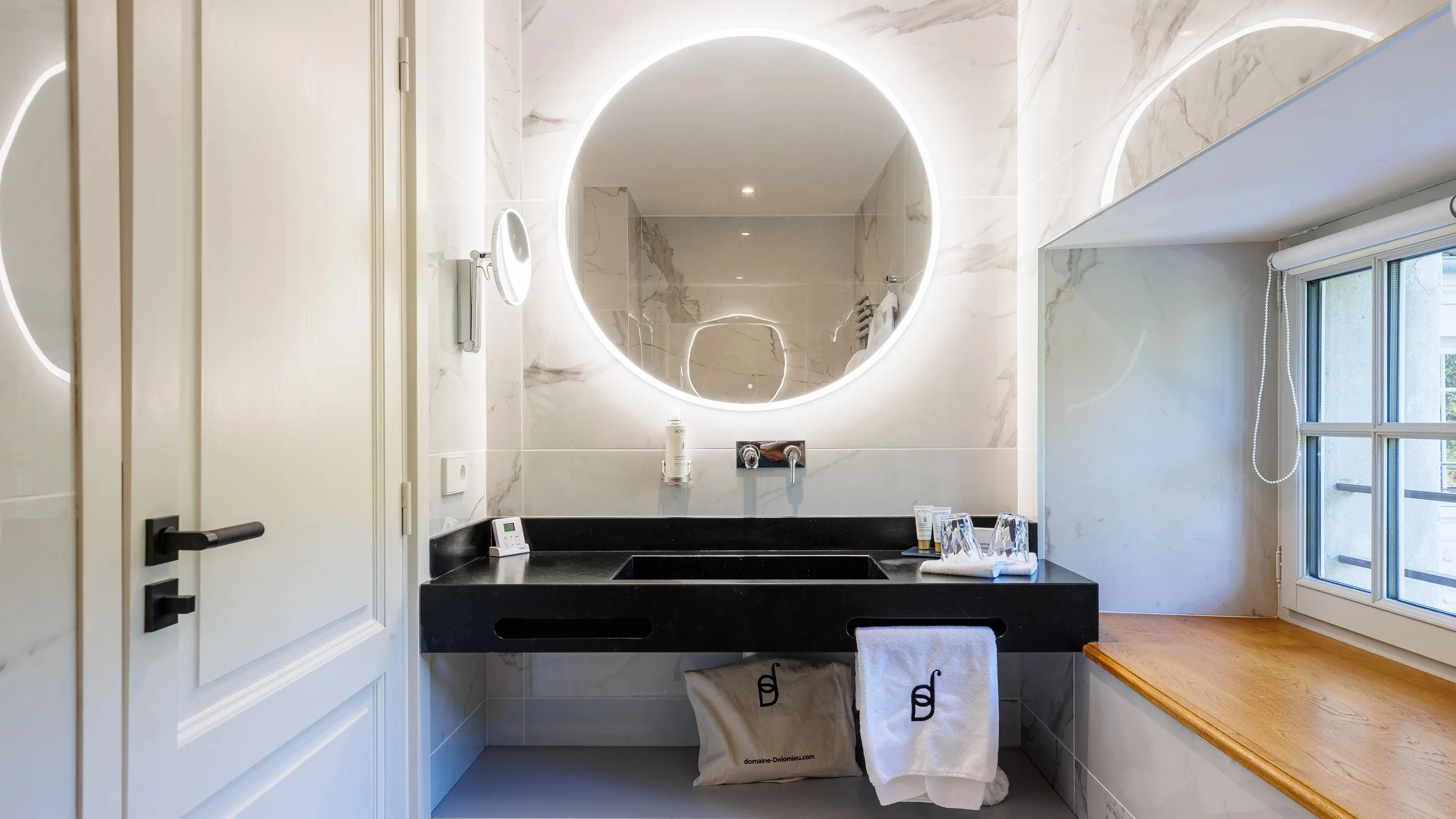 Moderne Badezimmer mit Doppelwaschbecken, beleuchtetem Rundspiegel und Fenster mit Jalousie