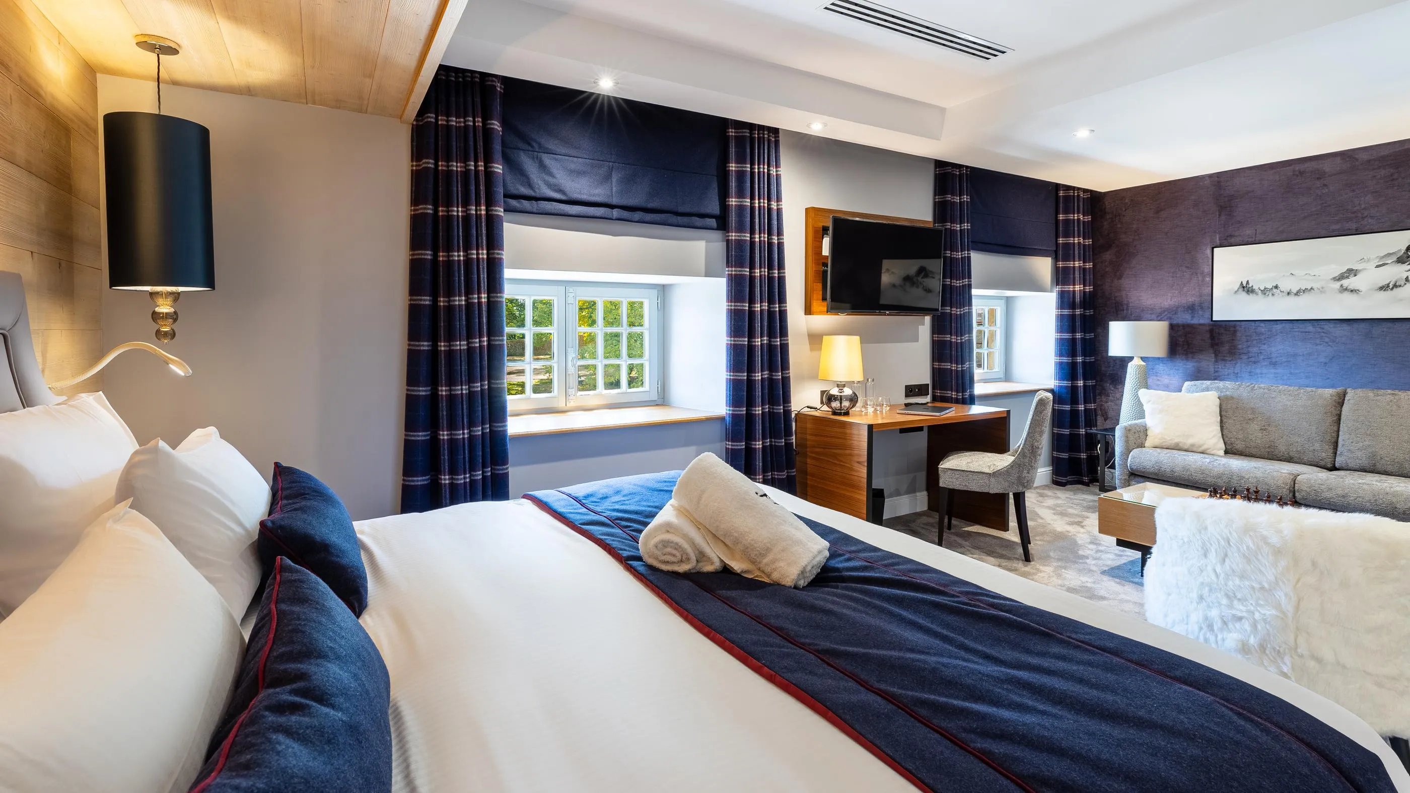 Chambre d'hôtel avec lit double, sofa, bureau, télévision et fenêtres donnant sur un jardin