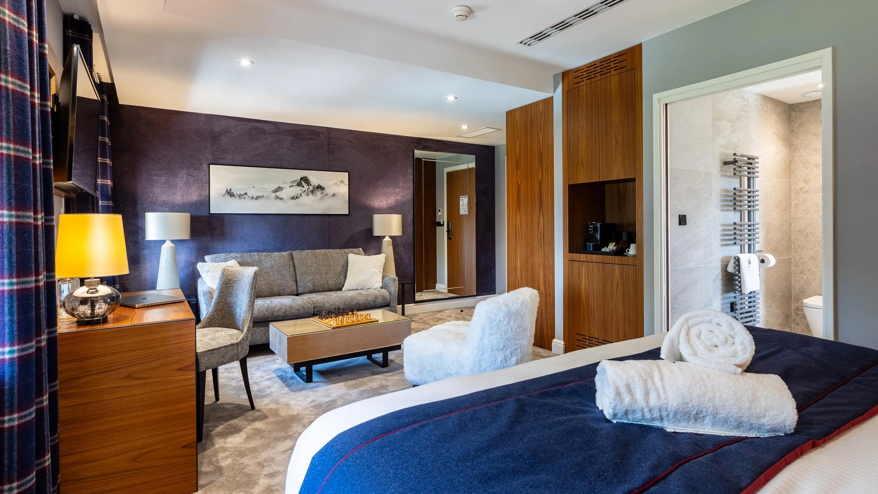Chambre d'hôtel moderne avec lit, canapé, table basse, bureau et salle de bain visible à l'arrière-plan