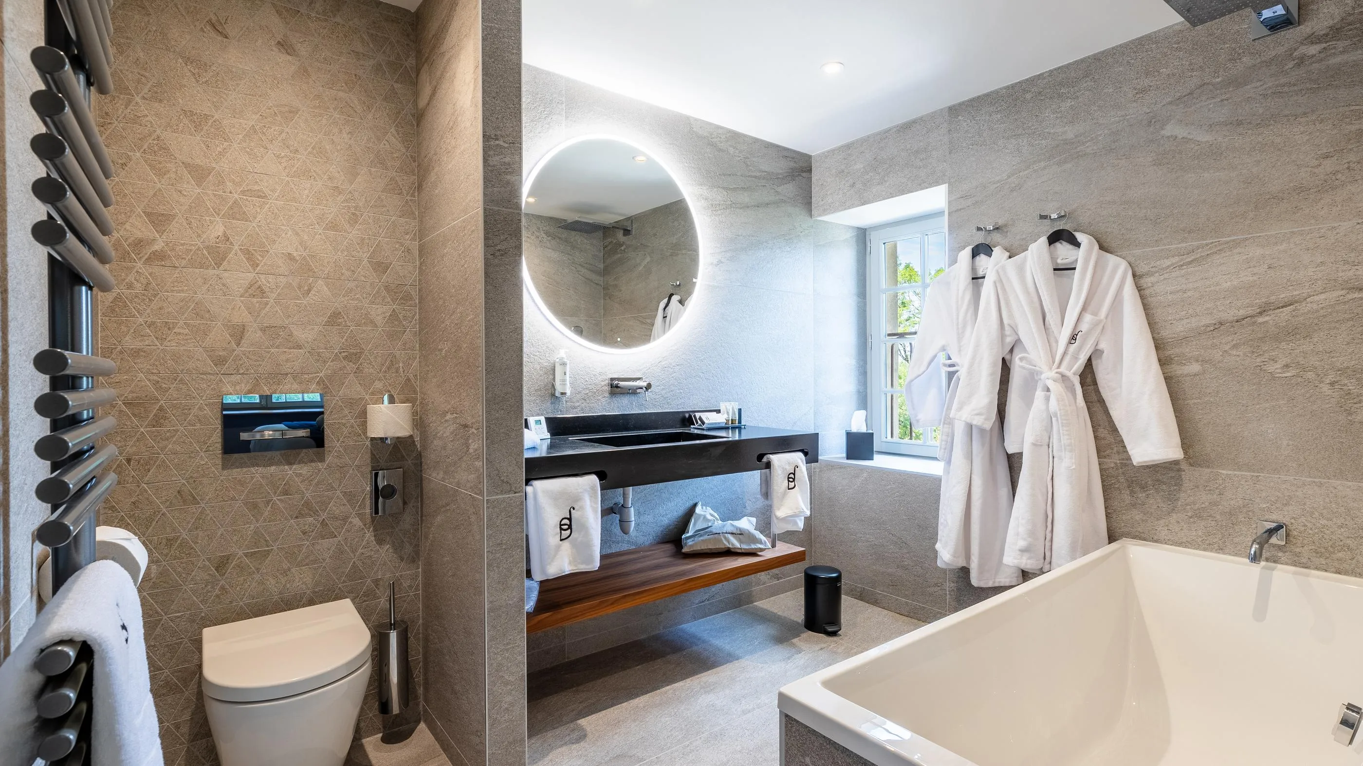 Salle de bain moderne avec baignoire, toilettes, lavabo, miroir rond et peignoir blanc accroché