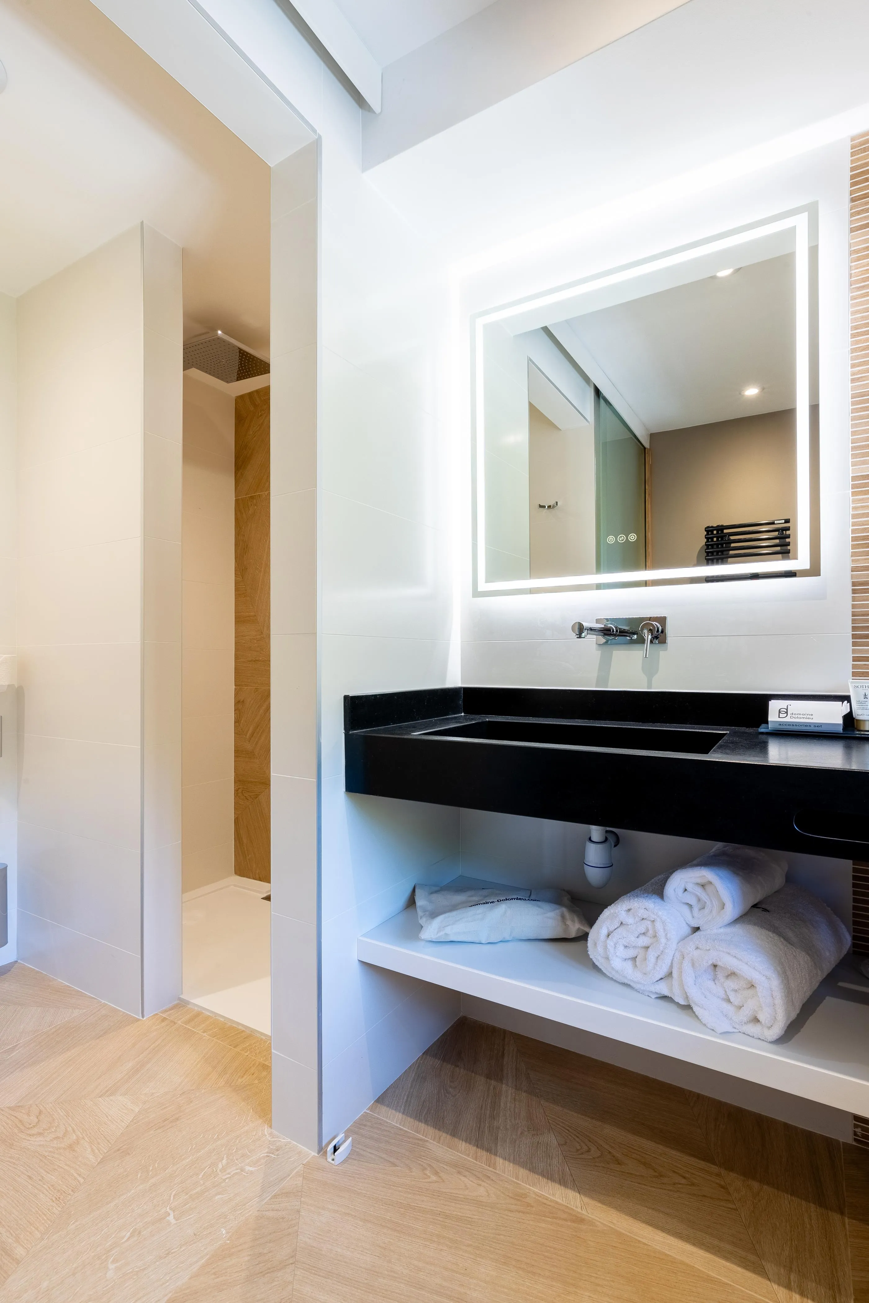 Moderne Badezimmer mit schwarzem Waschbecken, beleuchtetem Spiegel und weißen Handtüchern auf einem Regal
