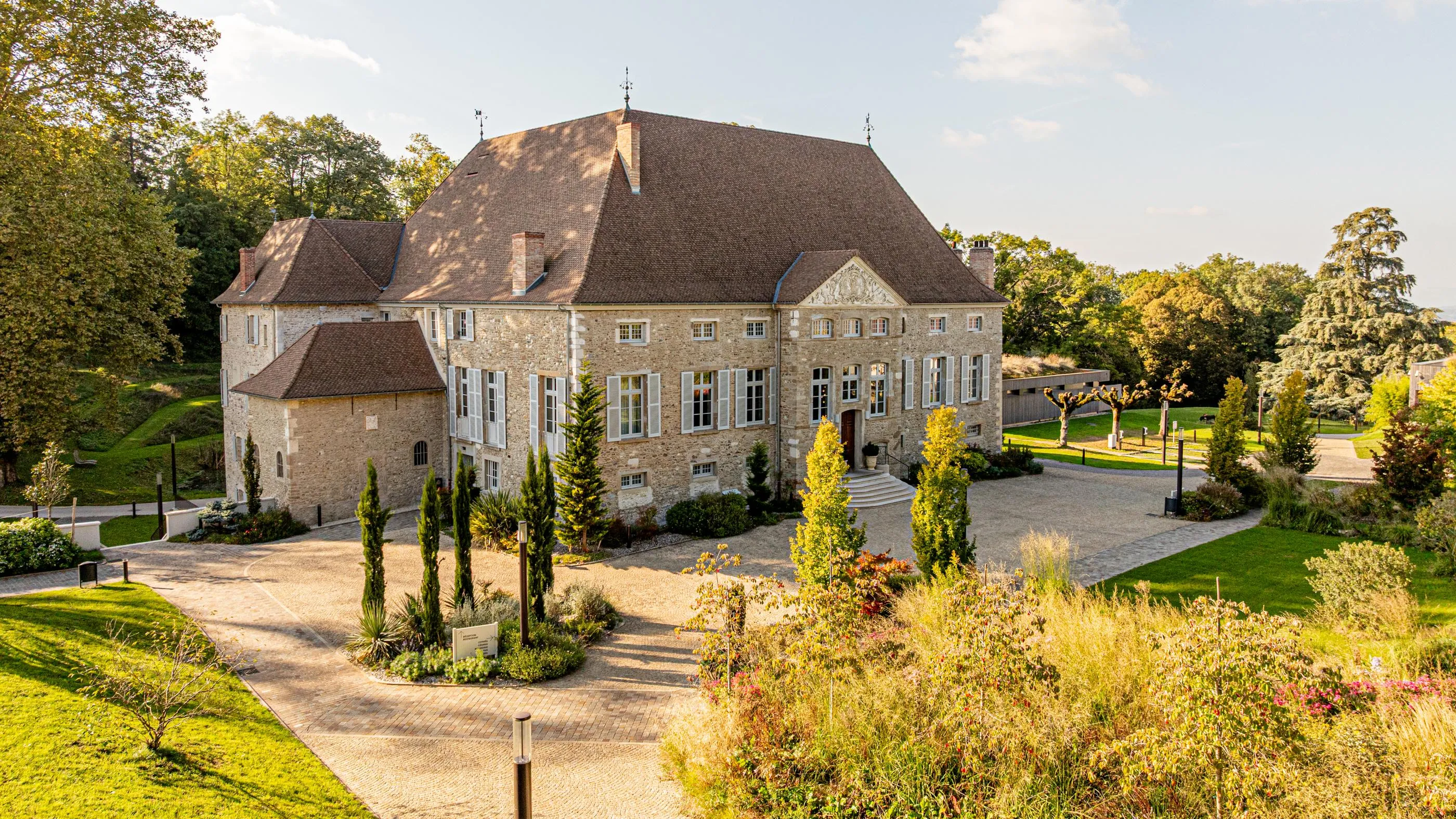 Maison en pierre avec toits en ardoise entourée d'un jardin paysager et d'arbres