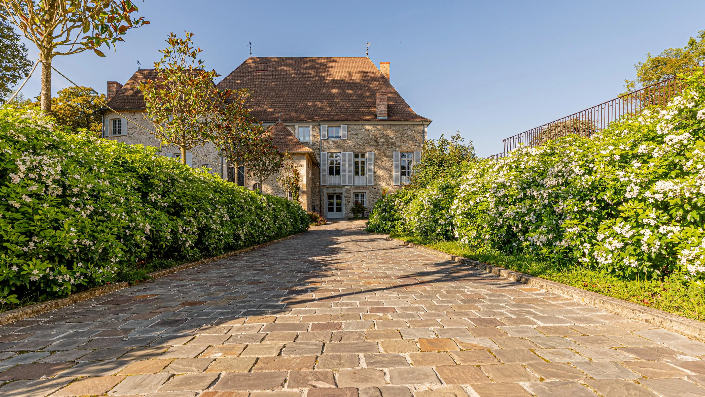 Maison en pierre avec toit en tuiles et jardin fleuri bordé d'un chemin pavé