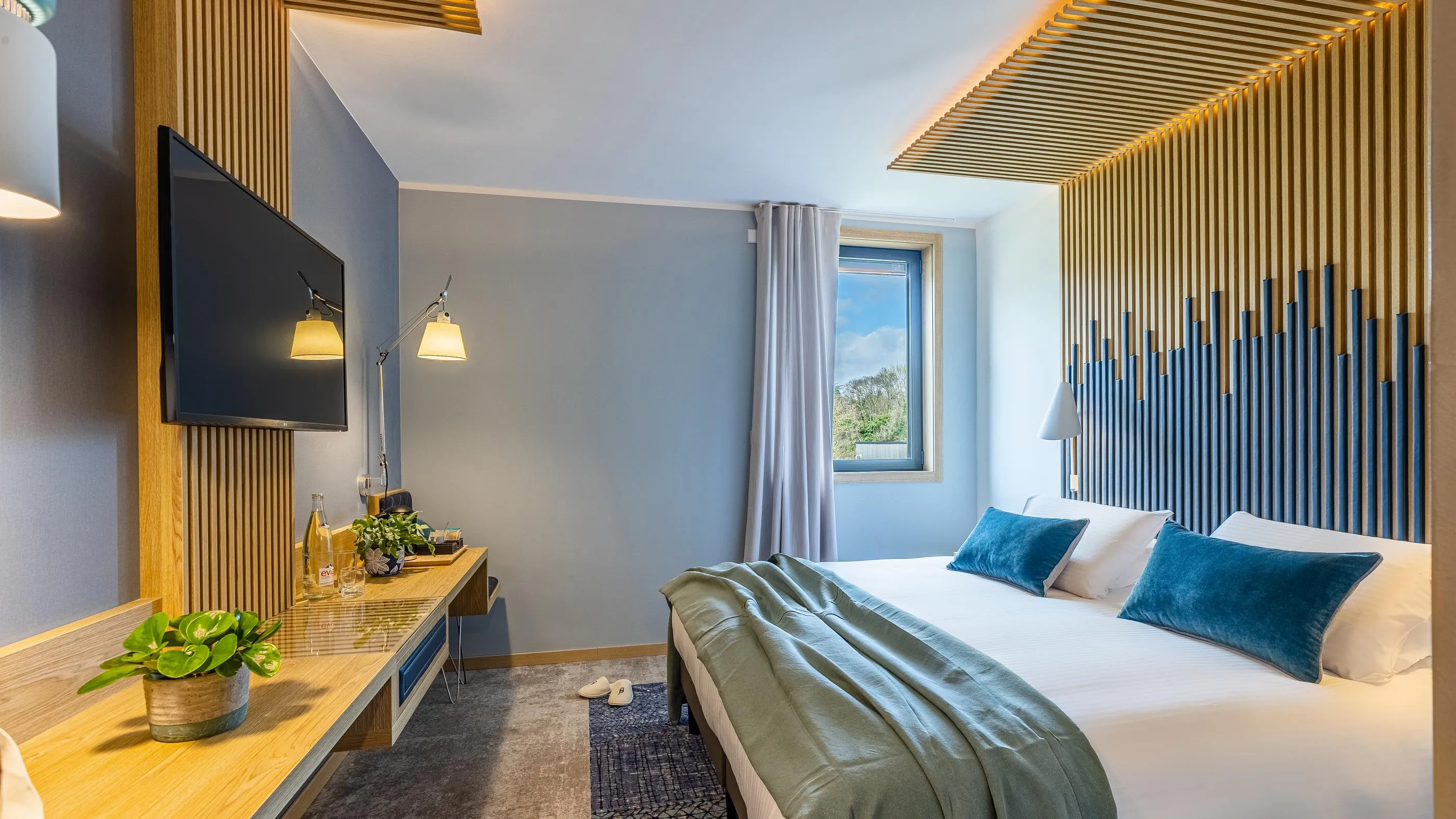 Chambre d'hôtel moderne avec un lit double, une télévision à écran plat, un bureau et une fenêtre laissant entrer la lumière naturelle