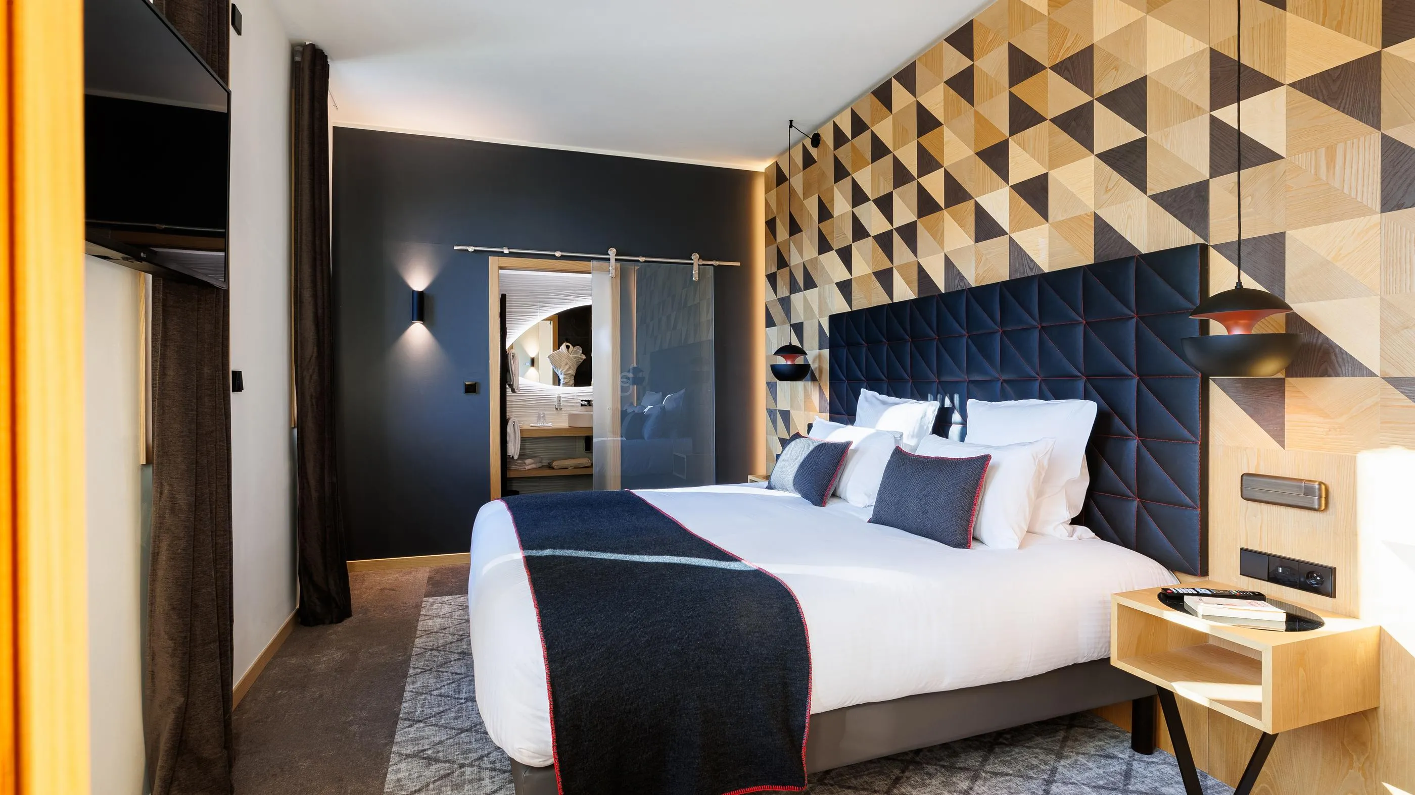 Chambre moderne avec un lit double, une tête de lit en velours bleu foncé et un mur décoré de motifs géométriques en bois clair et foncé