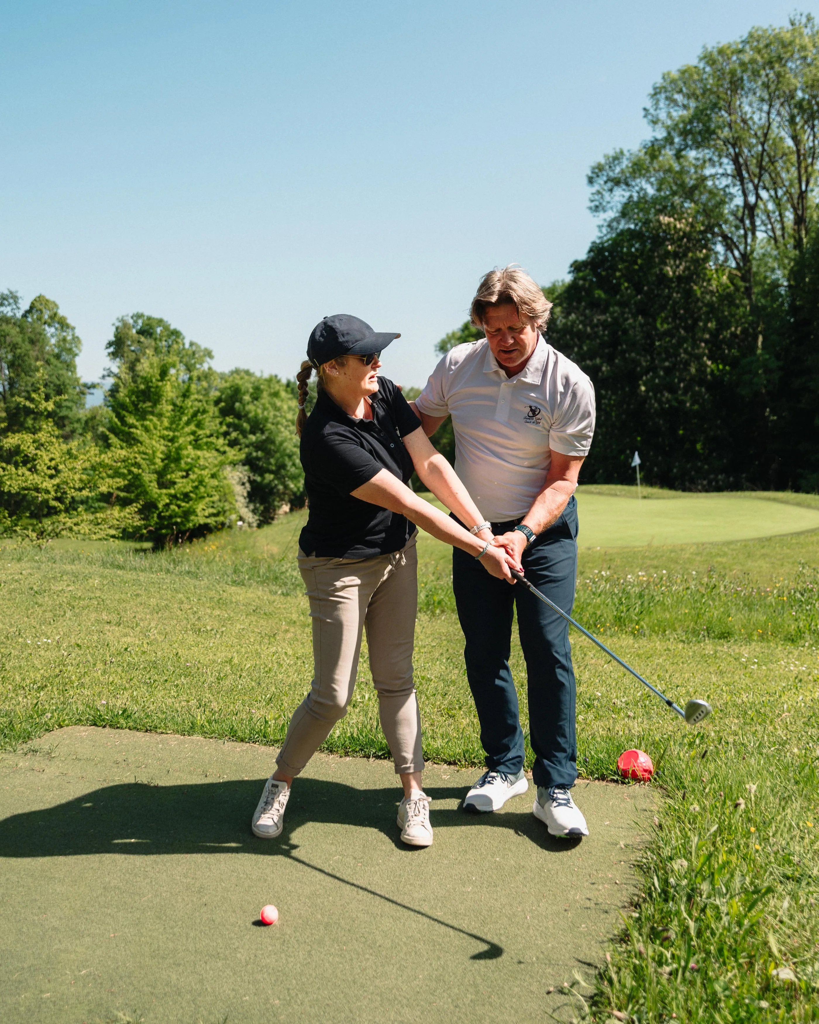 Deux personnes sur un green de golf, l'une aidant l'autre à ajuster sa posture de putt