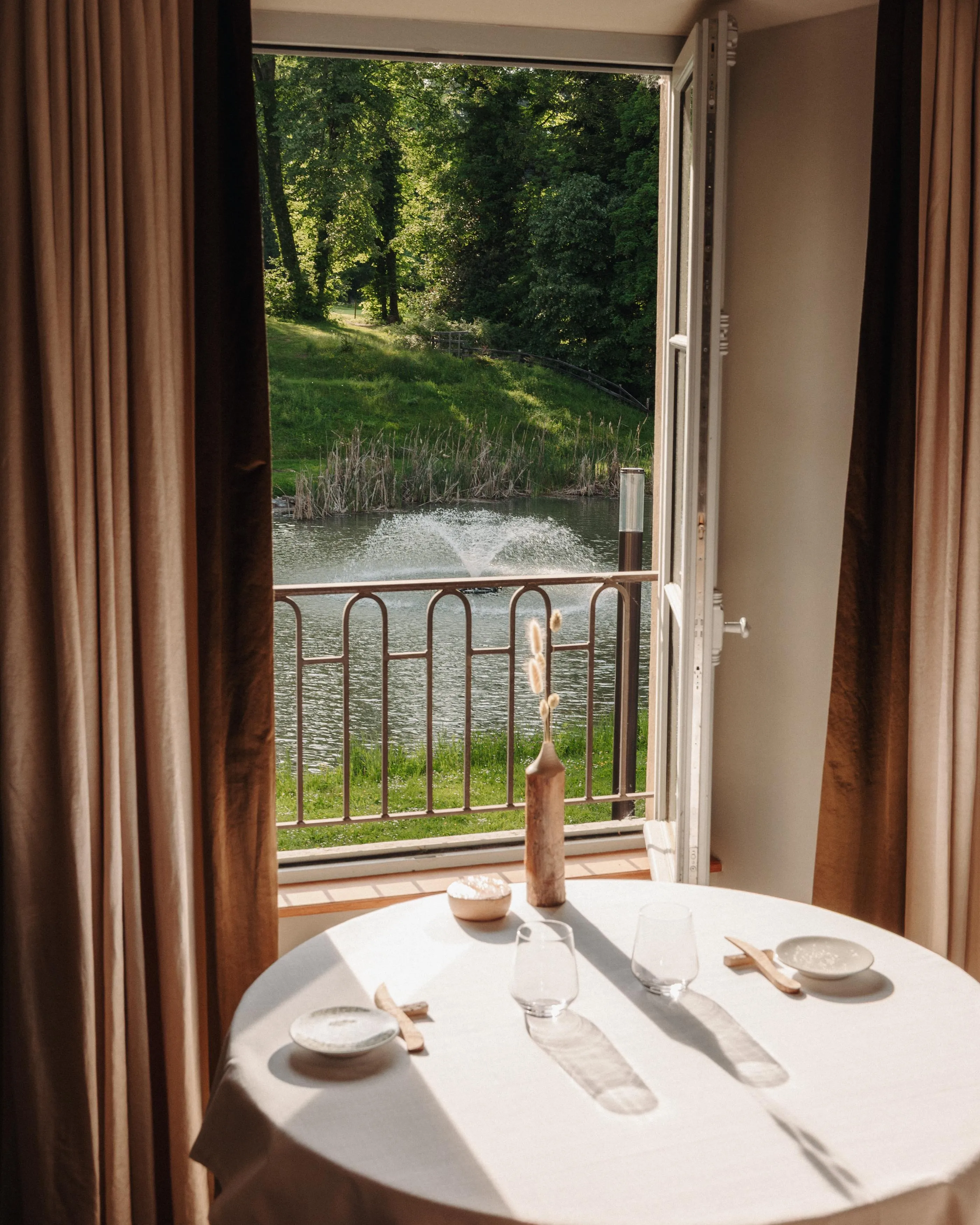 Table dressée avec verres, couverts et petits bols, vue sur un lac et des arbres à travers une porte-fenêtre ouverte