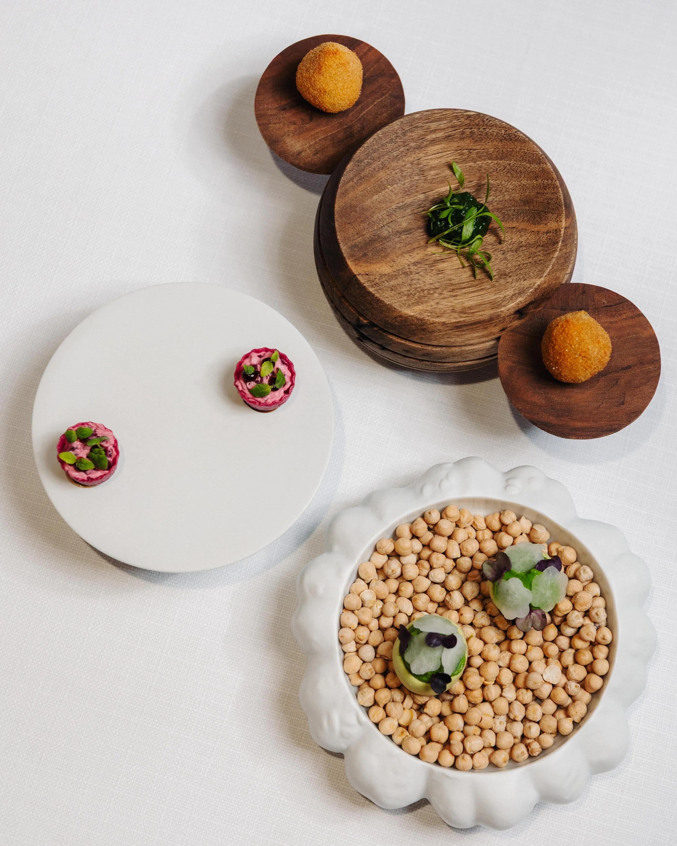 A tray with dishes containing meatballs, vegetables, and seeds, arranged on a white tablecloth.