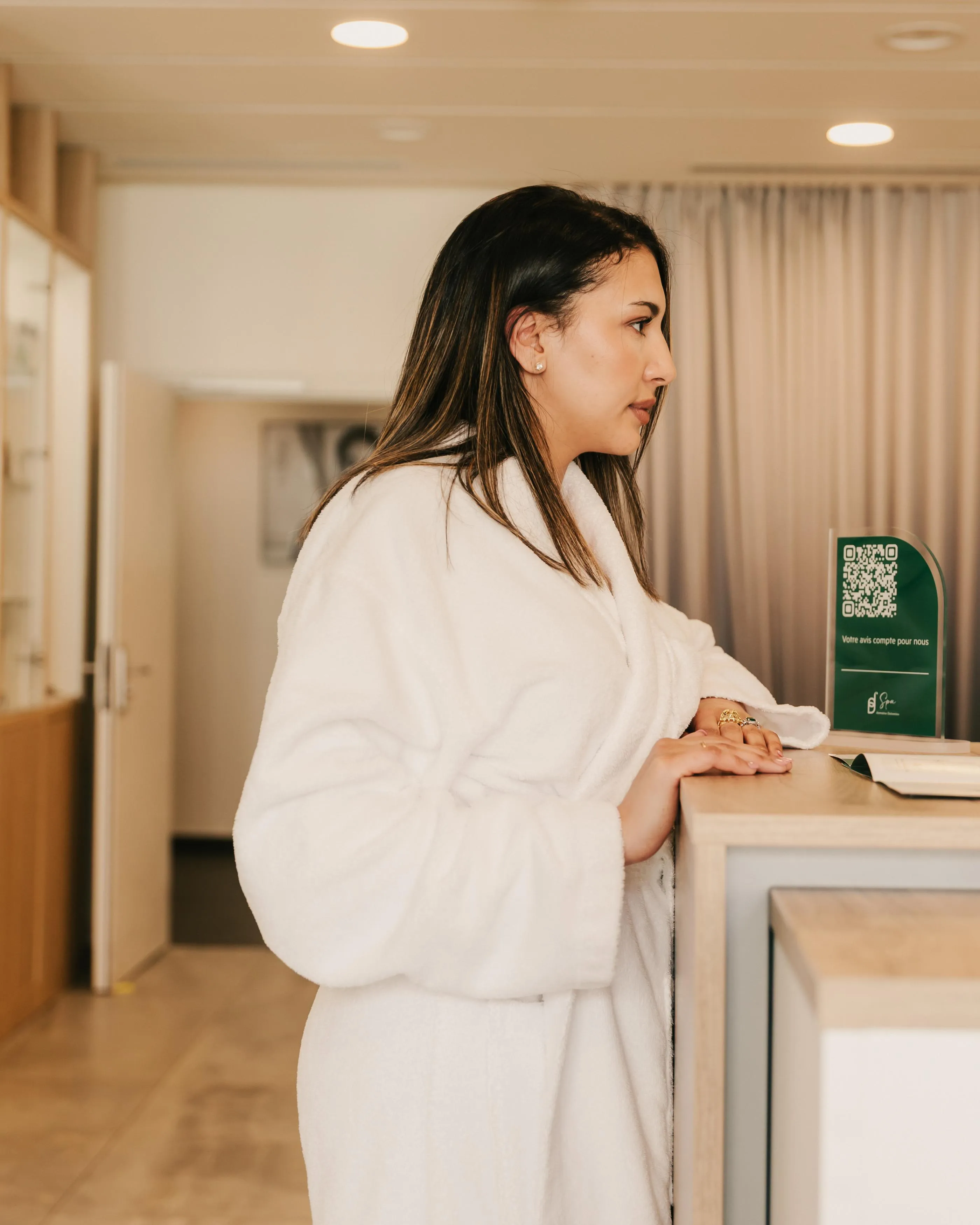 Woman in a white bathrobe standing behind a counter with a QR code holder