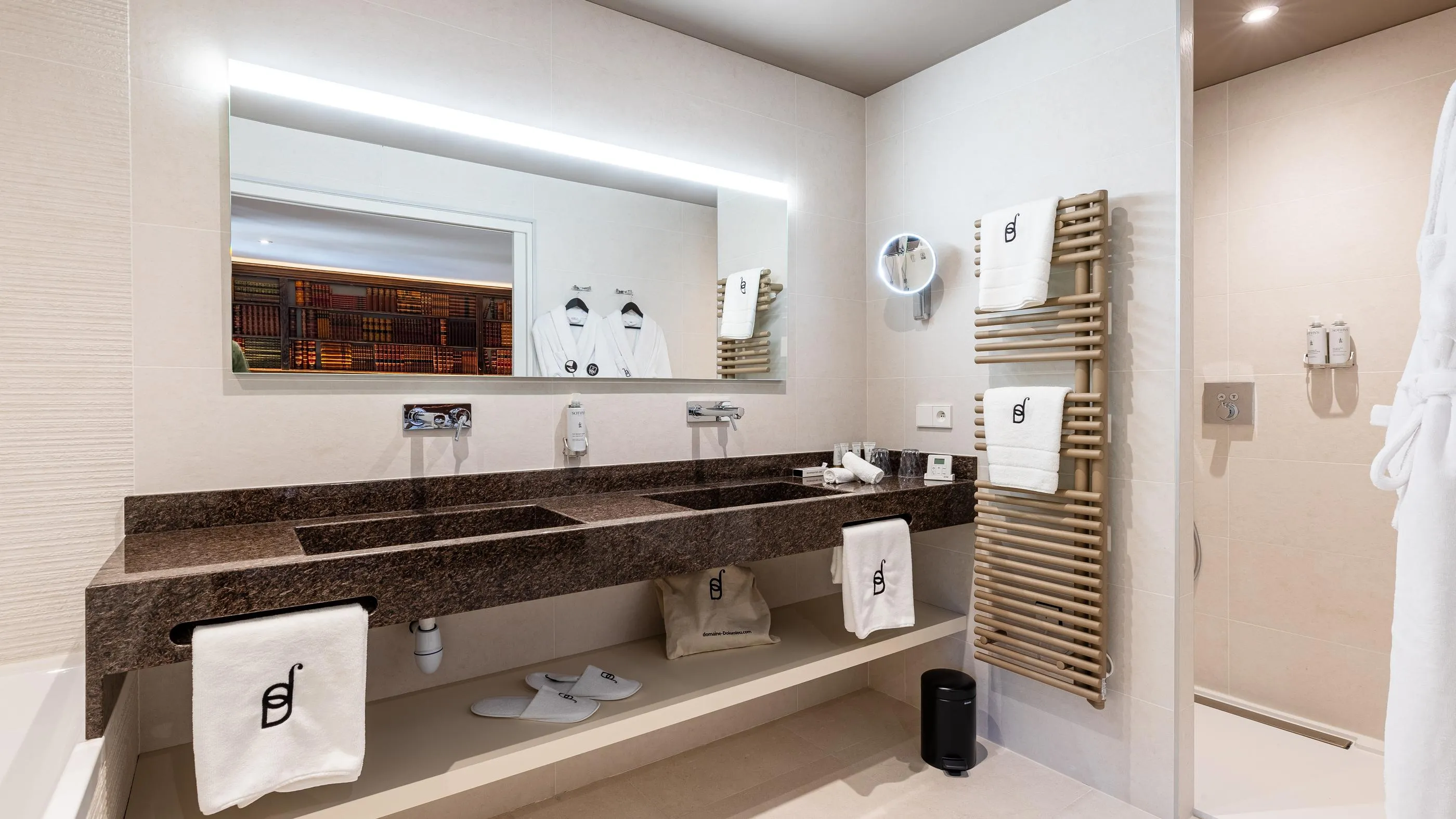 Modernes Badezimmer mit Doppelwaschbecken, Spiegel, aufgehängten Handtüchern und Bademänteln sowie einer Seifenablage an der Wand