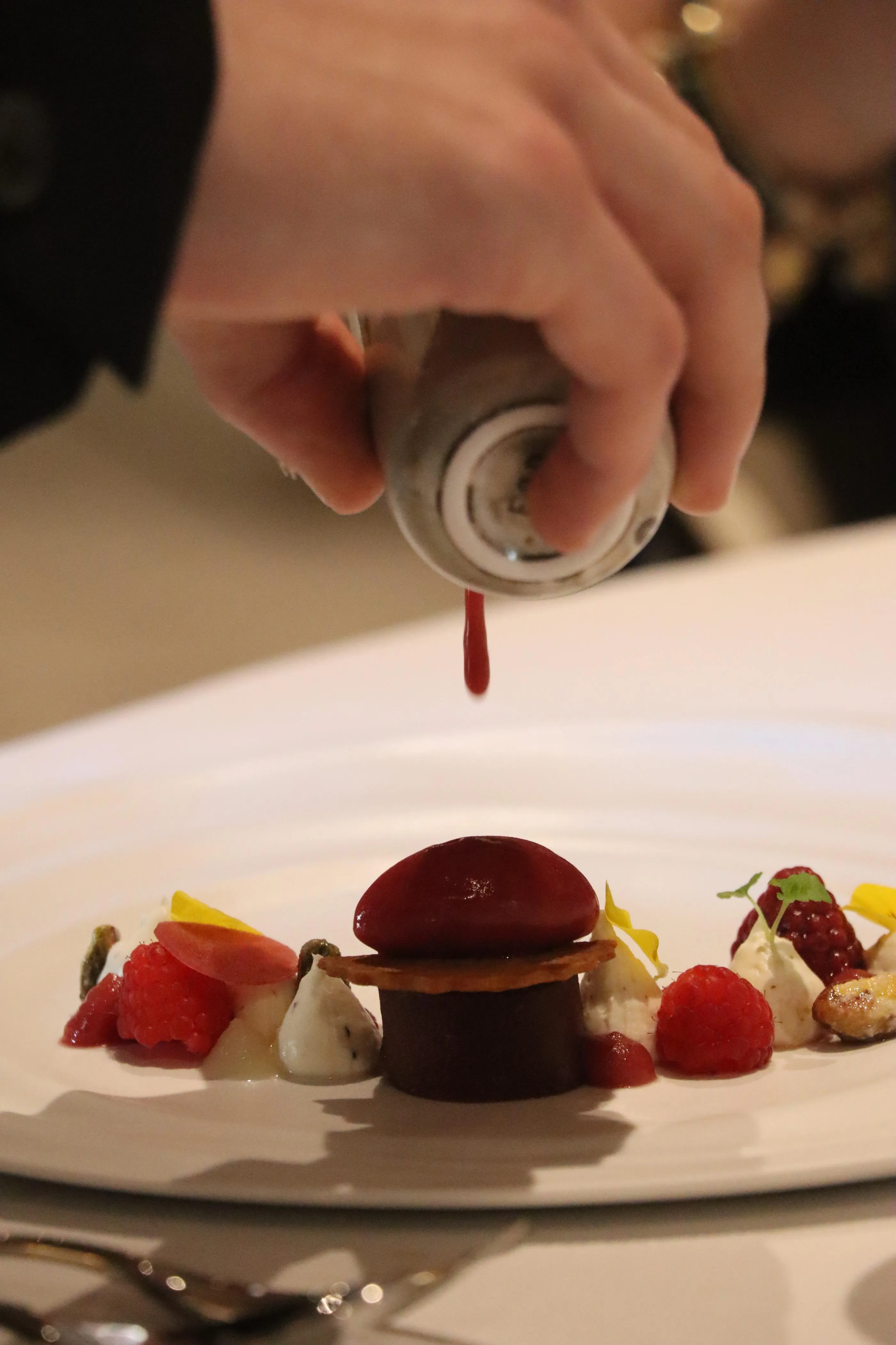 A person holds a piping bag and decorates a dessert made of fruits and toppings on a skewer.